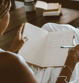 A black woman writes in a notebook, enjoying a calm indoor setting with natural light.